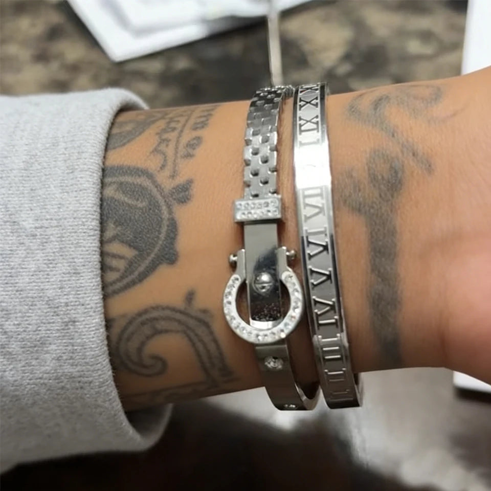 Roman Numeral Stainless Bracelet 2pcs Set an einer Hand mit Tattoos getragen, ein Armband mit einem Hufeisen und das andere mit römischen Zahlen.